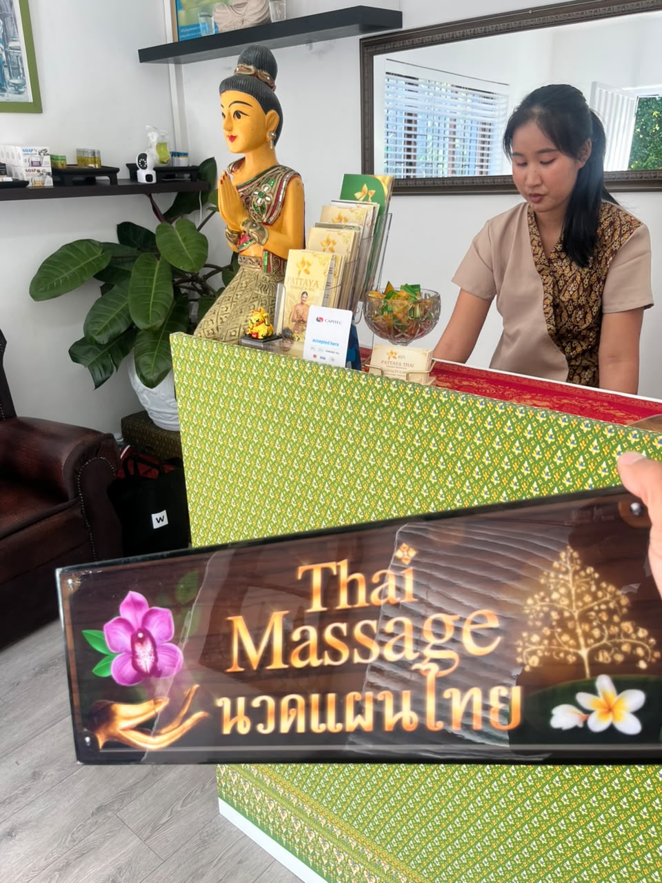 Thai therapist welcoming guests at the green-patterned reception desk