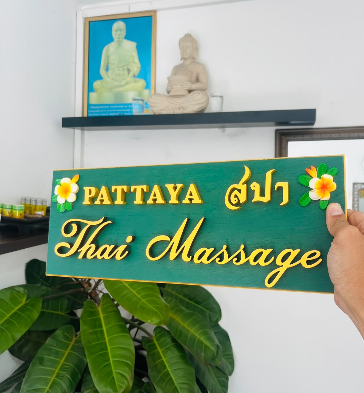 Hand holding the green and gold Pattaya Thai Massage signature signboard