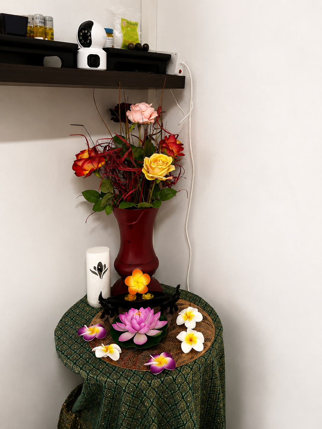 Thai silk draped table with a pink lotus, frangipani blooms, candle and floral vase in the treatment room corner
