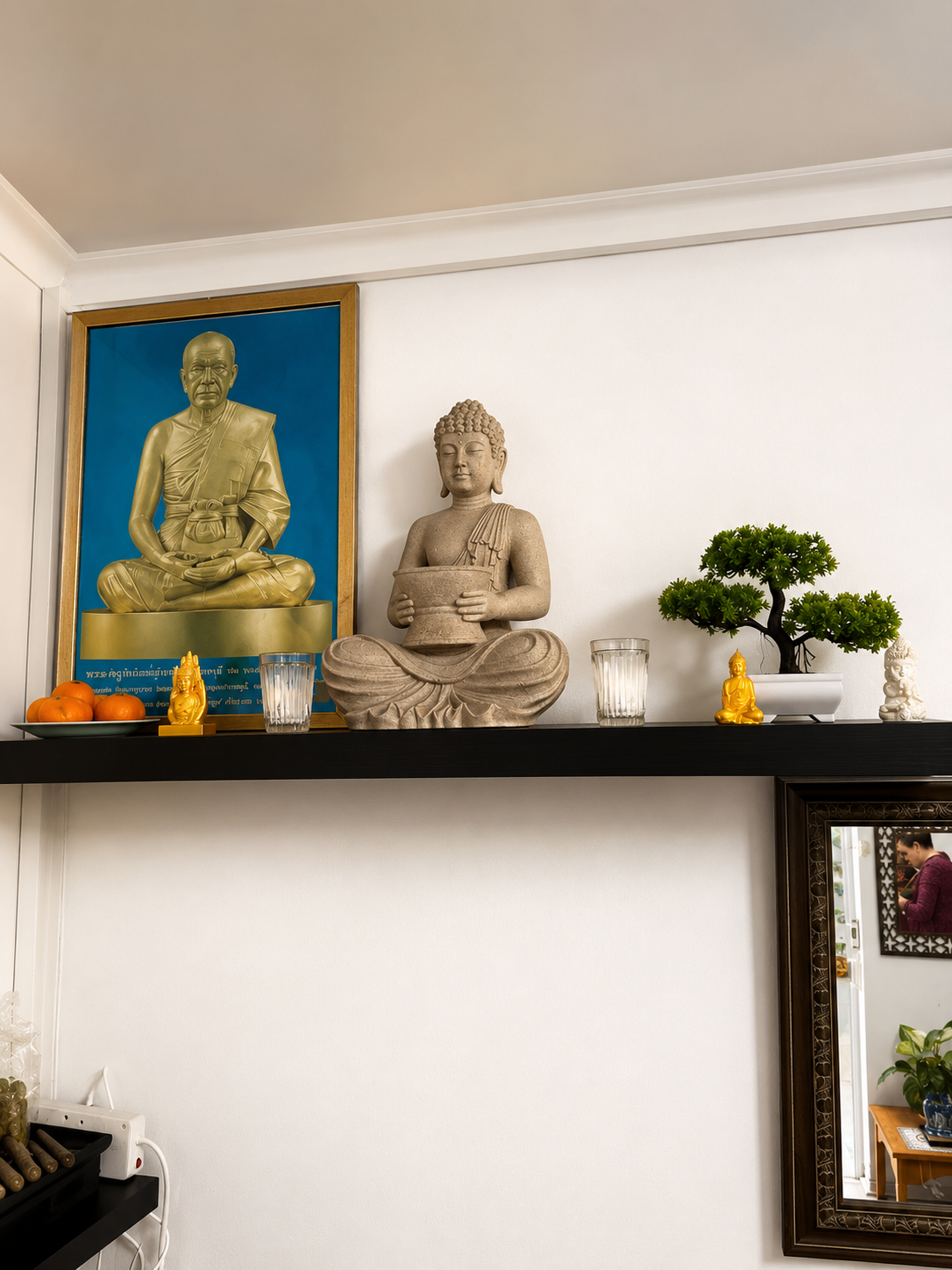 Stone Buddha statue, gilded monk portrait and bonsai arranged on a dark shelf above the spa waiting area